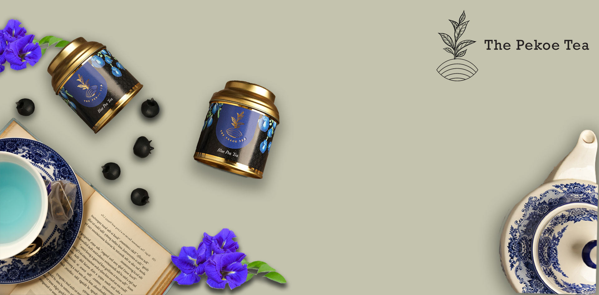 The Pekoe Tea Blue Pea Tea packaging with golden lids, fresh butterfly pea flowers, blueberries, and a cup of vibrant blue herbal tea in a blue-white teacup set.