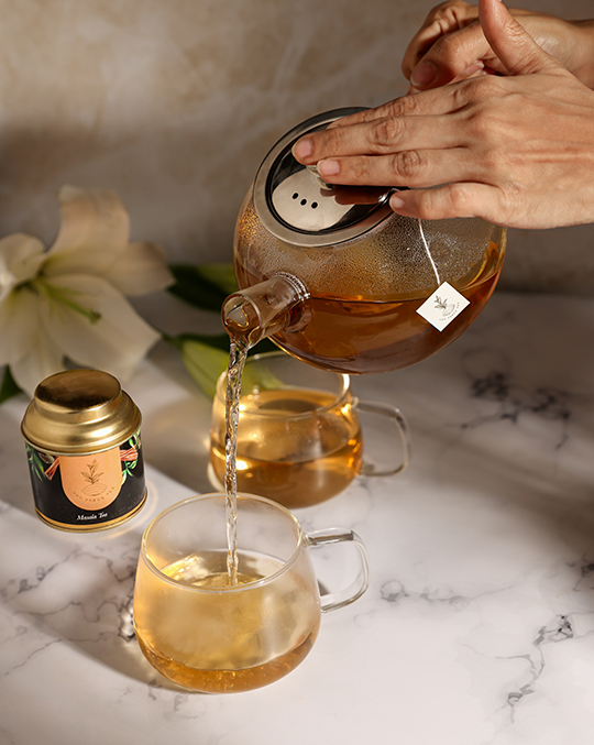A hand pouring Pekoe Masala Tea from a serving pot